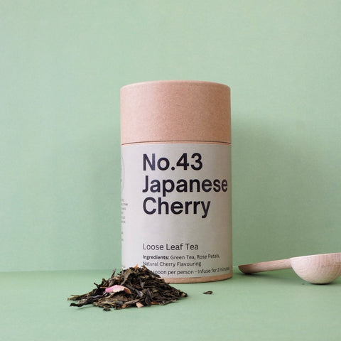 A cylindrical container labeled 'No.43 Japanese Cherry Loose Leaf Tea' with a spoon and scattered tea leaves in the foreground.