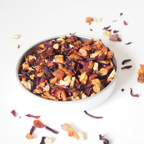 A bowl of spiced apple loose fruit tea showing the dried fruit, scattered on a white background