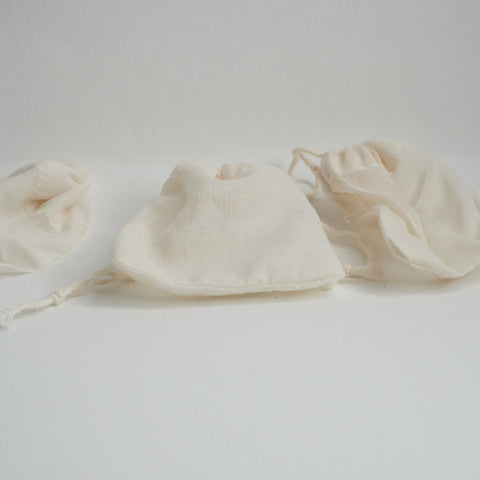 Three white reusable cotton teabags laid out on a light surface.