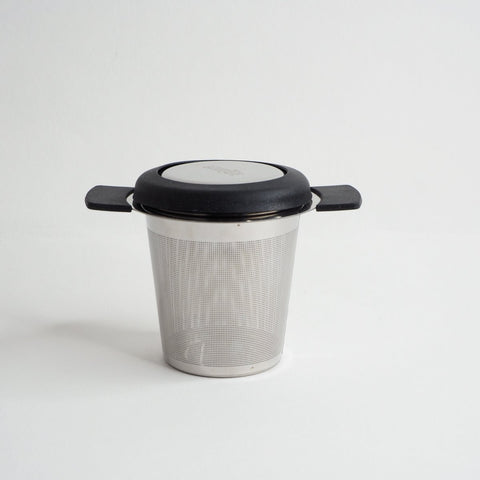 A stainless steel cup infuser for loose leaf tea with a black lid and handle, displayed against a white background.