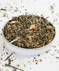 A white bowl filled with dried herbal tea leaves and spices, with a blend of green and brown colors.