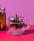 Two glass teapots with fruit infusions on a pink background