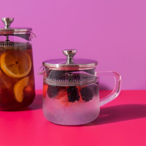Two glass teapots with fruit infusions on a pink background