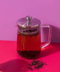 Clear glass teapot with silver lid on a pink background