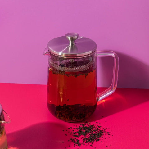 Clear glass teapot with silver lid on a pink background
