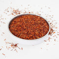 A swallow dish of Rooibos Herbal Tea from online teashop Teaspoon Tea Co.  The short bright loose leaves of Rooibos are light orange and red.  This looks a very tasty caffeine-free tea. 