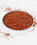 A swallow dish of Rooibos Herbal Tea from online teashop Teaspoon Tea Co.  The short bright loose leaves of Rooibos are light orange and red.  This looks a very tasty caffeine-free tea. 