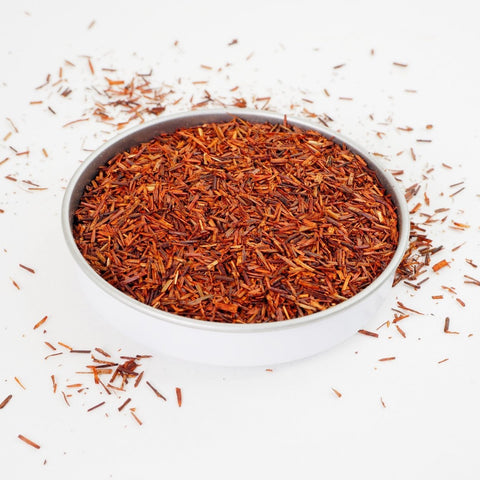 A swallow dish of Rooibos Herbal Tea from online teashop Teaspoon Tea Co.  The short bright loose leaves of Rooibos are light orange and red.  This looks a very tasty caffeine-free tea. 
