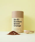 A cylindrical container labeled 'No.61 Rooibos Blood Orange' with loose herbal tea leaves scattered in front and a scoop to the side on a yellow background.