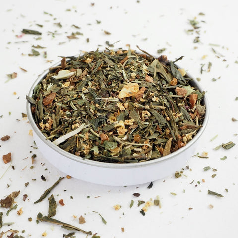 A white bowl filled with dried herbal tea leaves and spices, with a blend of green and brown colors.