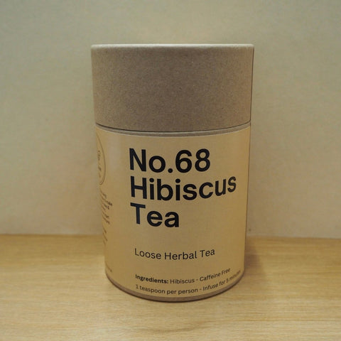 Cardboard container of No.68 Hibiscus Tea on a wooden surface with a beige background