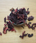 Dried hibiscus flowers in a small metal bowl on a wooden surface