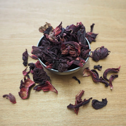 Dried hibiscus flowers in a small metal bowl on a wooden surface