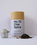 A cylindrical brown cardboard packaging labeled 'No.70 Chai Spice Loose Leaf Tea' with a silver tea ball and a pile of loose tea leaves in the foreground.