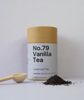A cylindrical container labeled 'No.79 Vanilla Tea' next to a wooden spoon with loose leaf tea scattered around it.