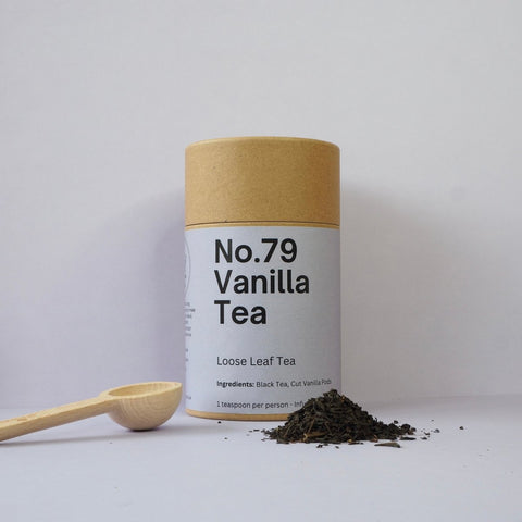 A cylindrical container labeled 'No.79 Vanilla Tea' next to a wooden spoon with loose leaf tea scattered around it.