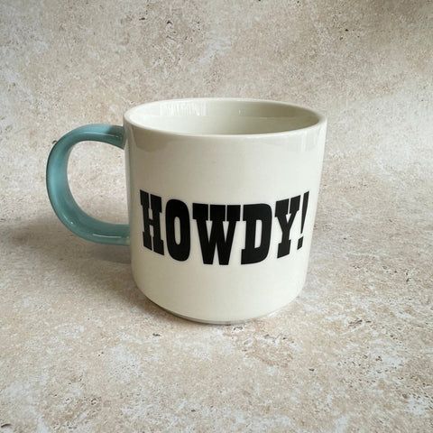 White mug with 'HOWDY!' printed on it, sitting on a textured surface.