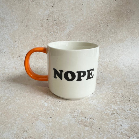 White mug with orange handle and 'NOPE' text on a gray surface