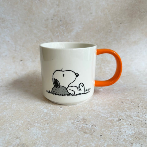 White mug with orange handle featuring a black and white illustration of Snoopy