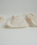 Three white reusable cotton teabags laid out on a light surface.