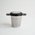 A stainless steel cup infuser for loose leaf tea with a black lid and handle, displayed against a white background.
