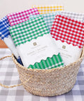 Colorful checkered tea towels in a woven basket on a checkered tablecloth.