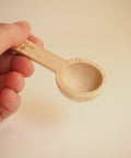 A hand holding a wooden measuring spoon for loose leaf tea or ground coffee