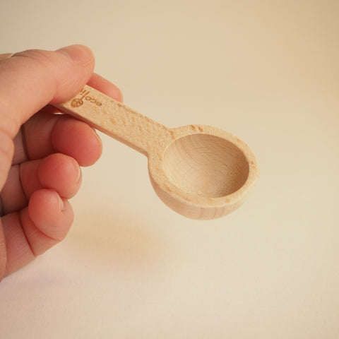 A hand holding a wooden measuring spoon for loose leaf tea or ground coffee